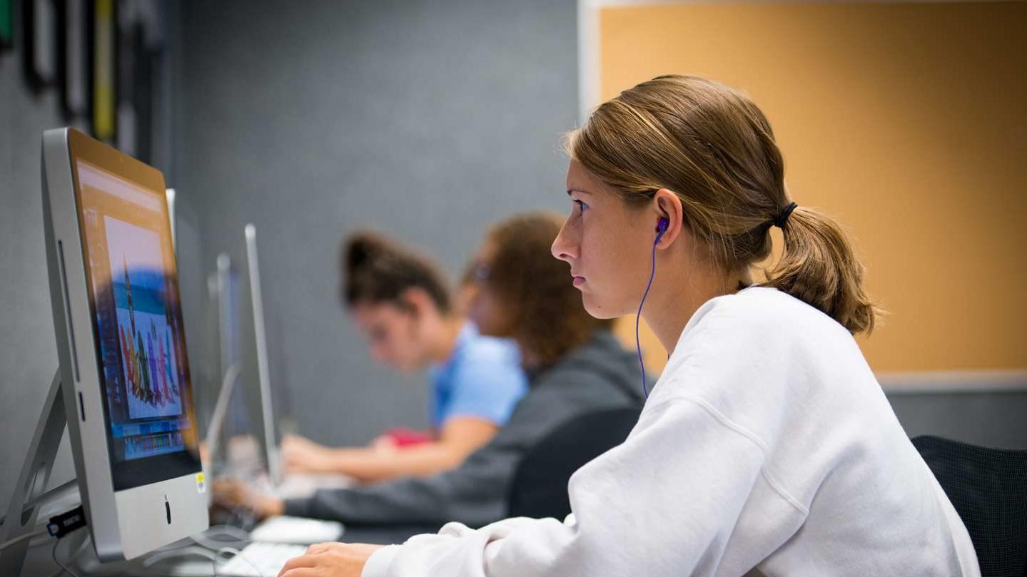 Graphic design student wearing a white sweater works in the design lab