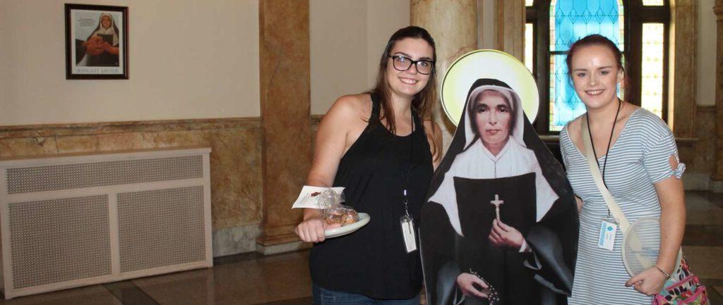 Two female student on each side of Flat Saint Mother Theodore Guerin smiling.