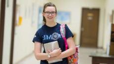 A female student holding her ipad and bookbag smiling.